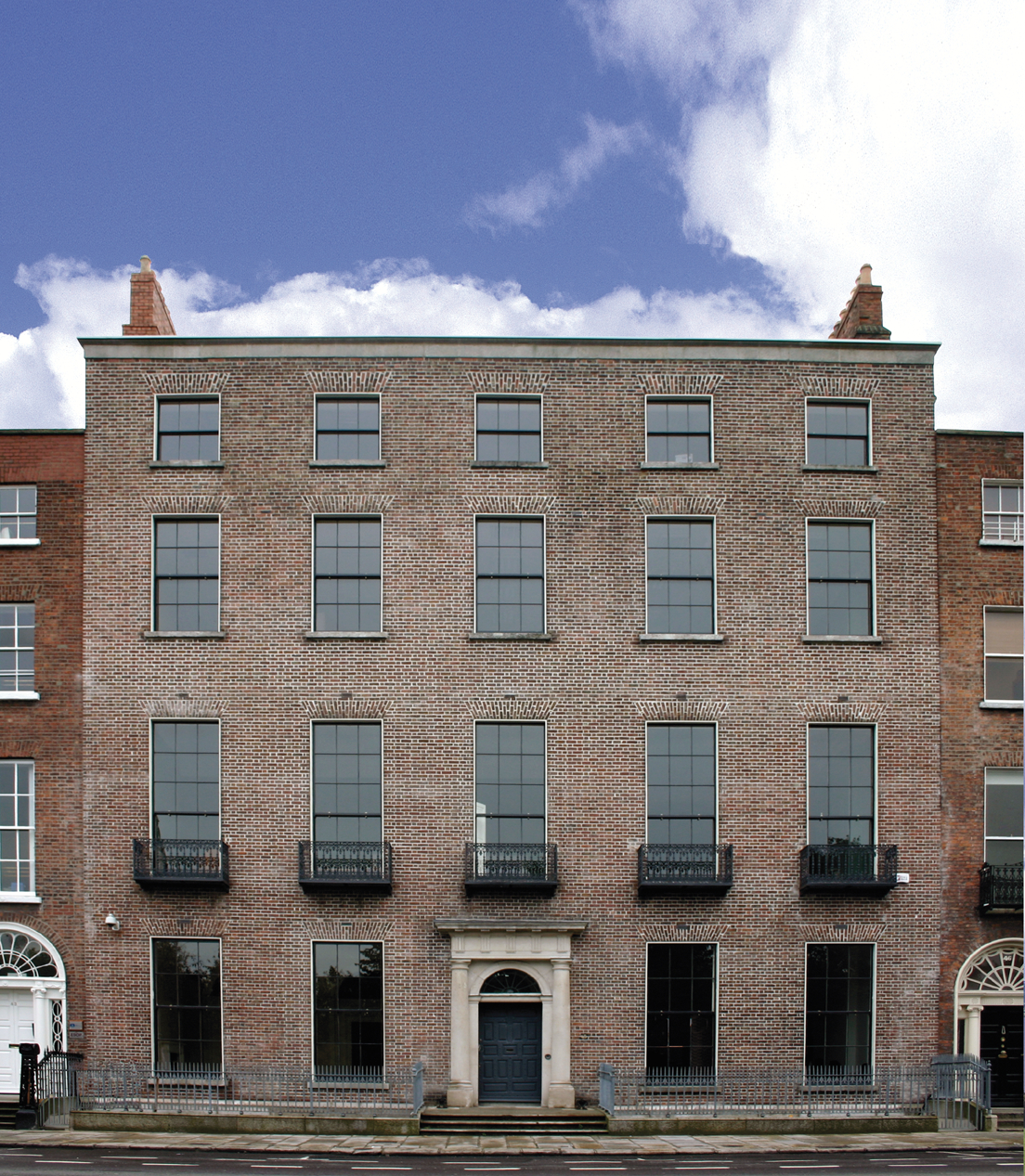 A large 4 storey red brick Georgian terraced house with blue sky and clouds