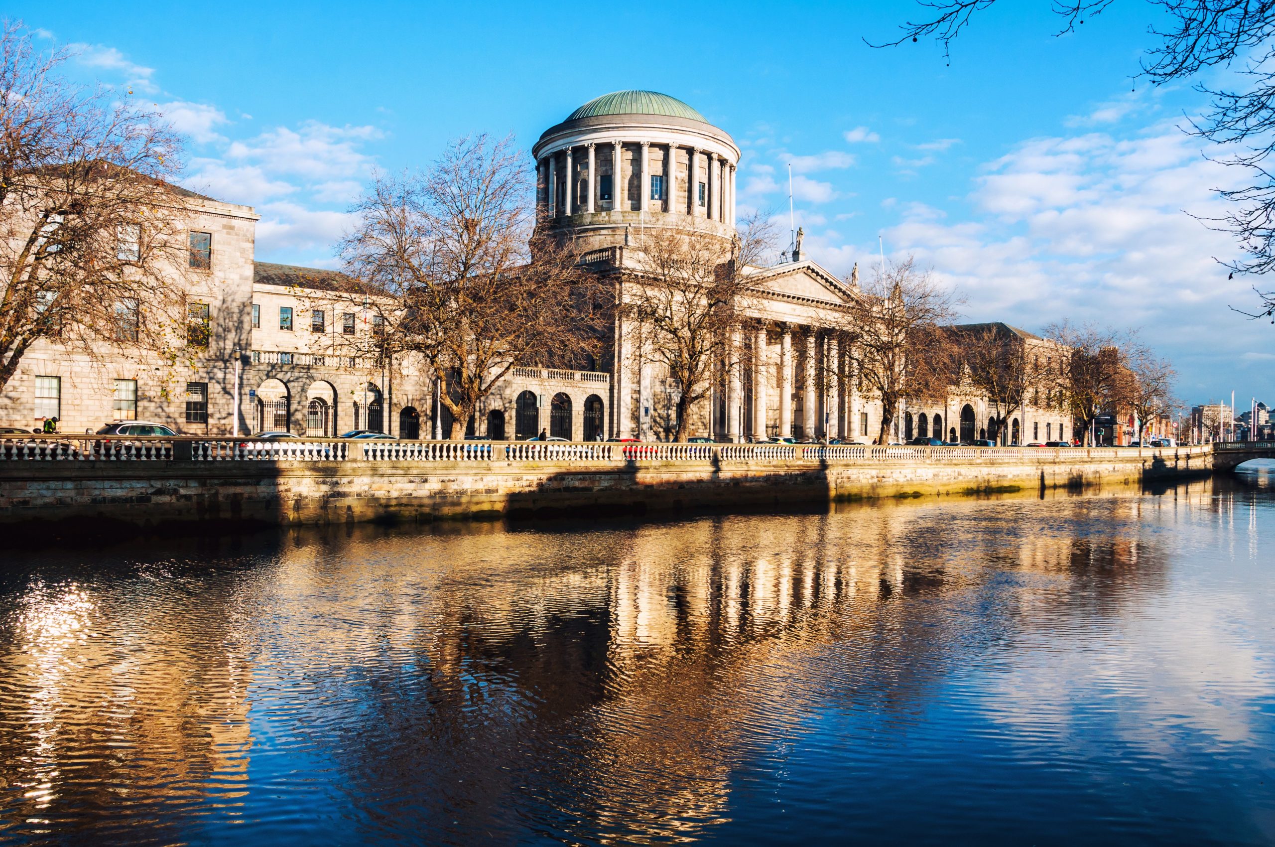 Building with classical architecture with Corinthian Columns and Dome on top. River with building reflection on the forefront.