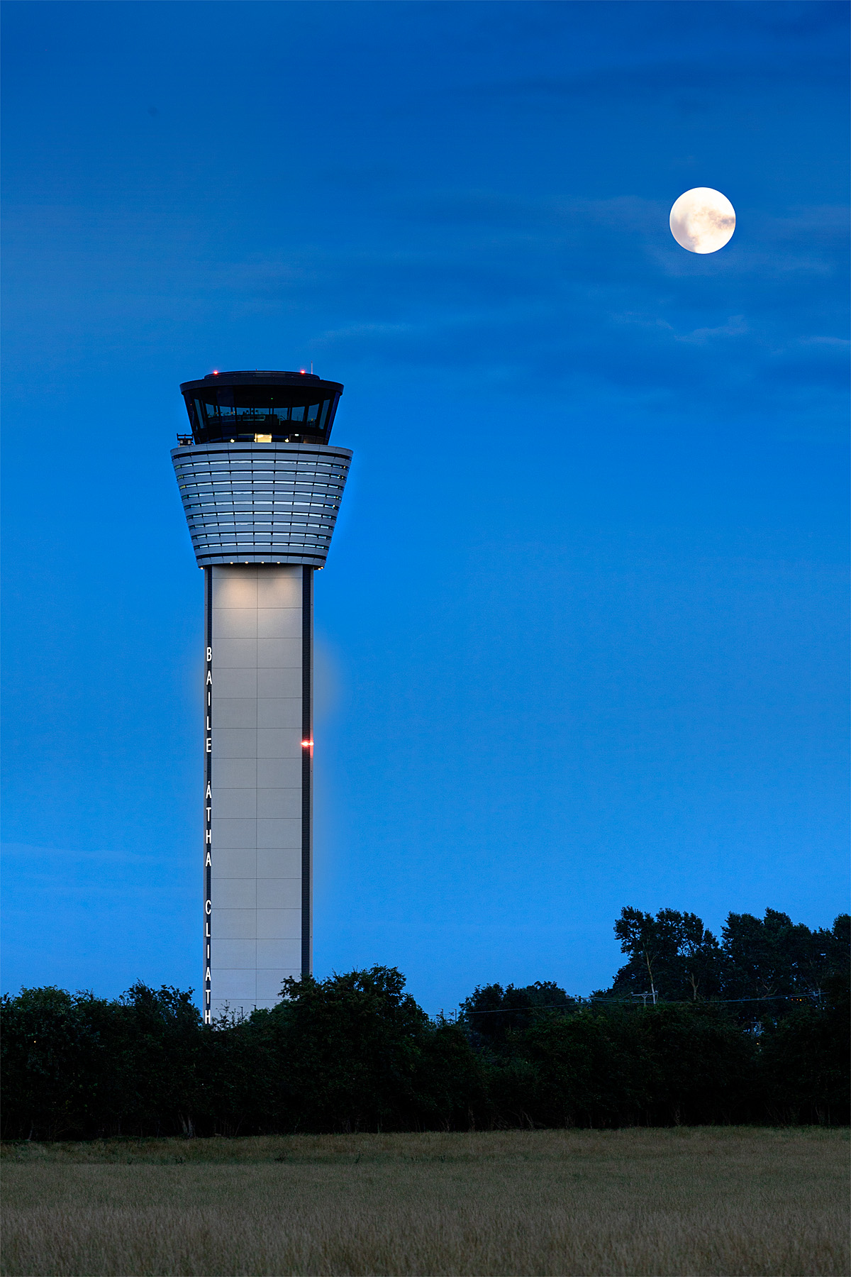 Full moon overlooking Dublin Air Traffic Control Tower against blue sky