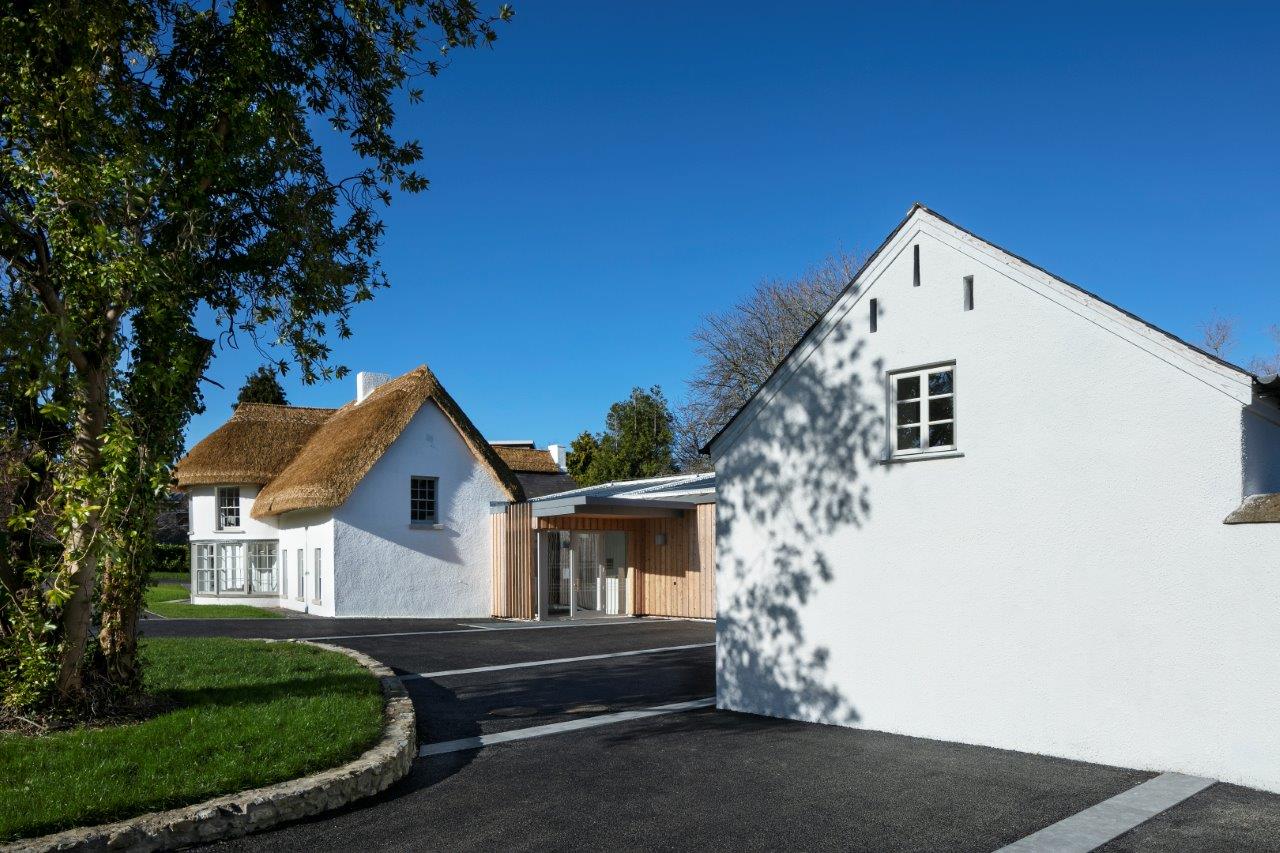 Side view of a white thatched cottage with timber cladded extension and landscaped drive