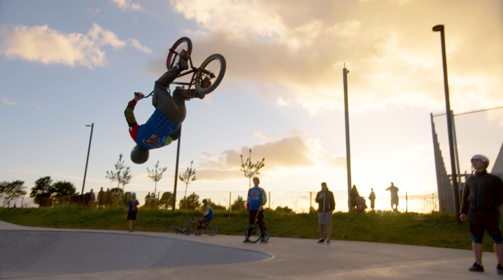 Cyclist doing a flip on a ramp at BMX park. Three young people watch in the background