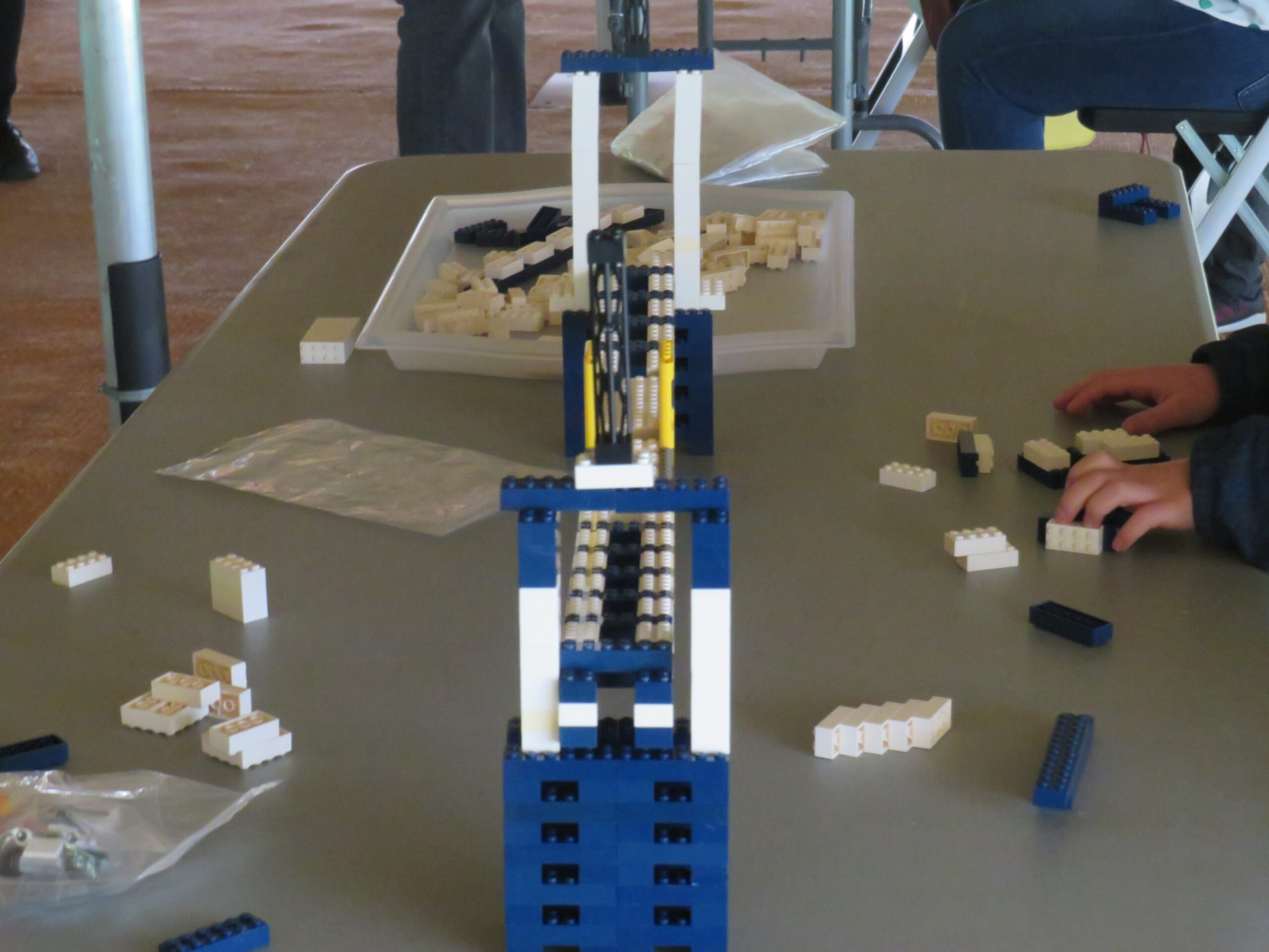 Bridge model made with white and blue lego pieces with loose lego pieces around it on a table