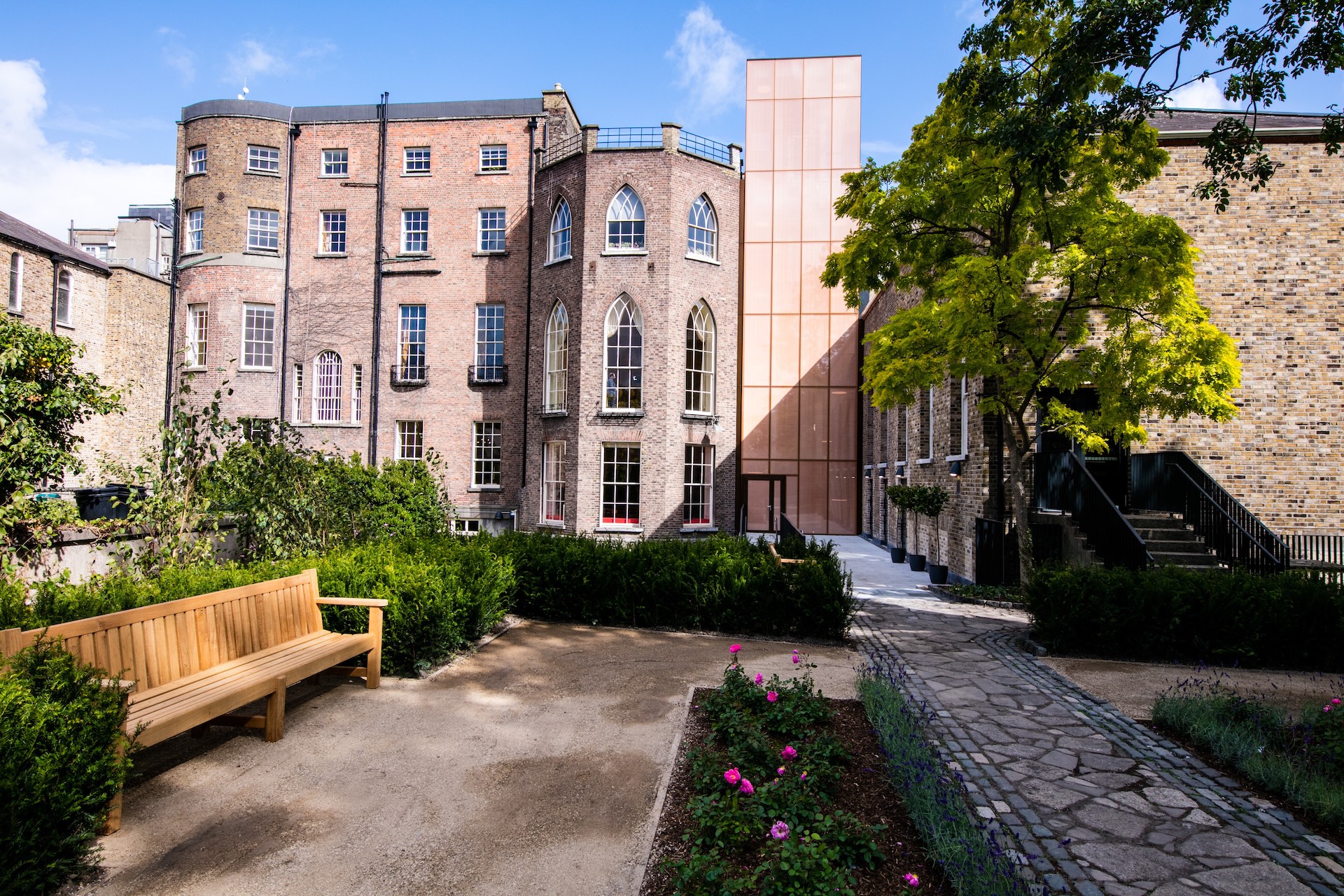A view from the MoLI Reader Garden showing the two grey brick Georgian buildings, the copper exterior of the lift addition and the grey brick Aula Maxima.