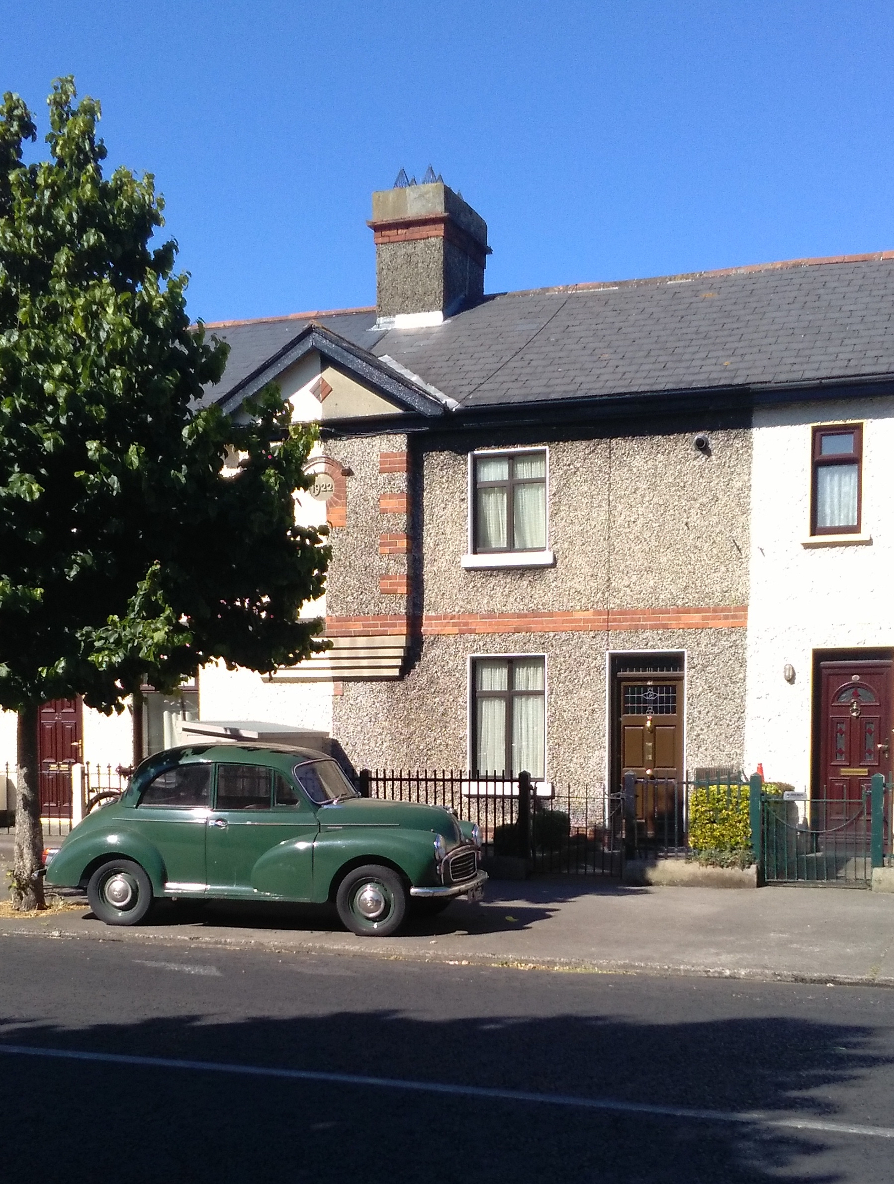 Street view of two storey house with chimney and a green vintage car in the front