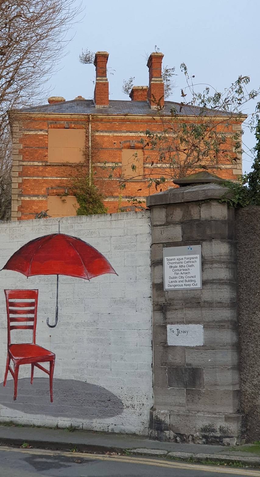Street mural depicting a red chair underneath a red umbrella in the foreground and derelict building in Stoneybatter
