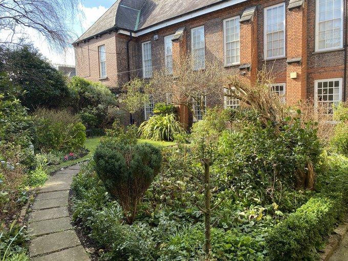 Garden with walkway to the left and various shrubs to the right and brick library in the background